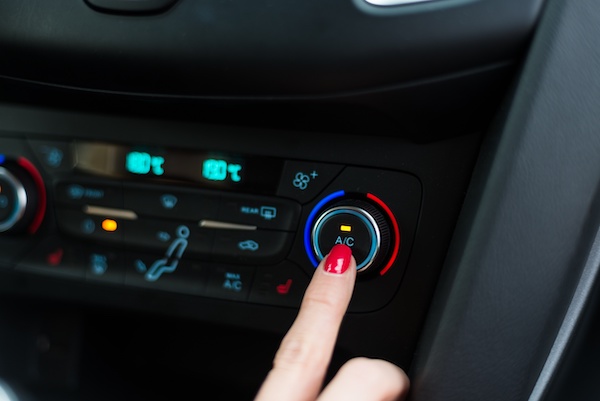 Woman's finger pressing on the A/C knob on the dashboard of a vehicle